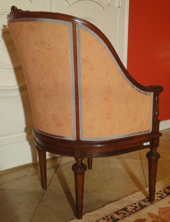 The gondola-shaped stained beechwood frame features a bow carving on the crest. A cushion of Fortuny upholstery is attached to the interior cane that surrounds a down cushion with buttons. The armrests are carved with acanthus leaves above columns