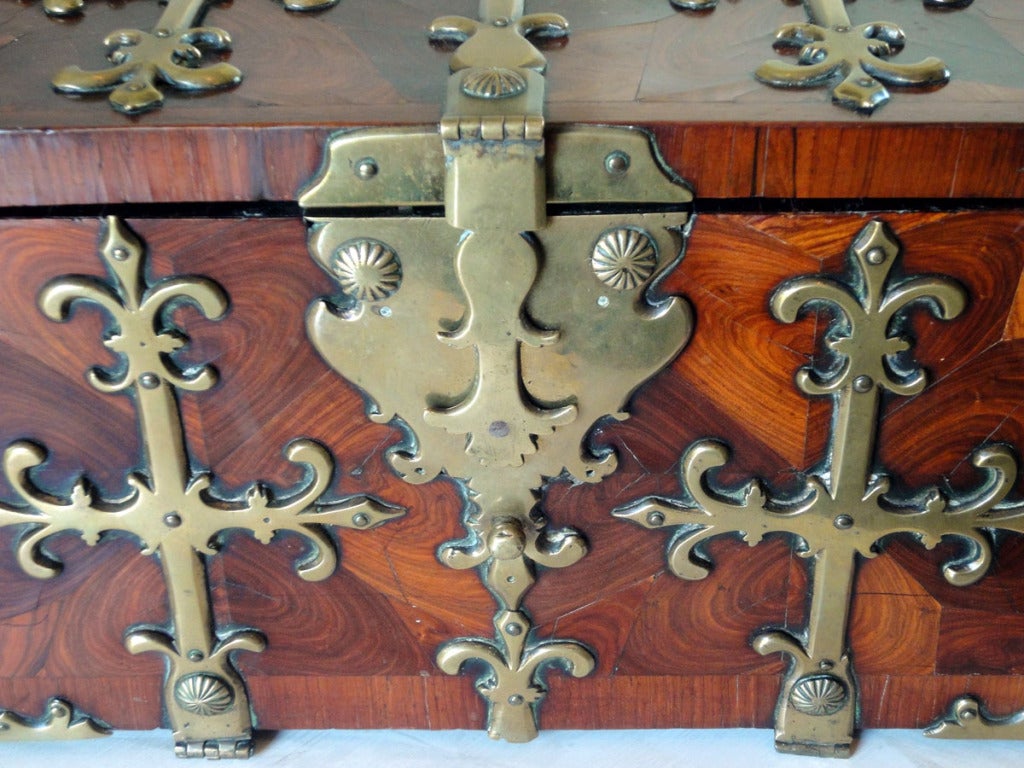 The surface of the box is oyster veneered with banding around the edge, & the front, back & ends repeat this design element. Fancy cut brass work is mounted to all the exterior flat surfaces & the pattern has a pseudo-fleur de lis design element.