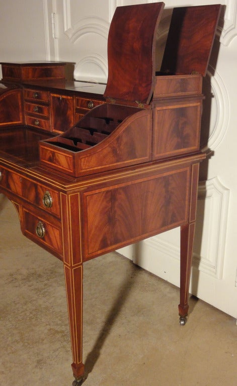 Unique Carlton House Style Desk with Sliding Writing Surface, Secret Compartments, & a Letter Slot. The desk has its original flame mahogany finish & note handsome banding & stringing. With original brass casters & drawer pulls.