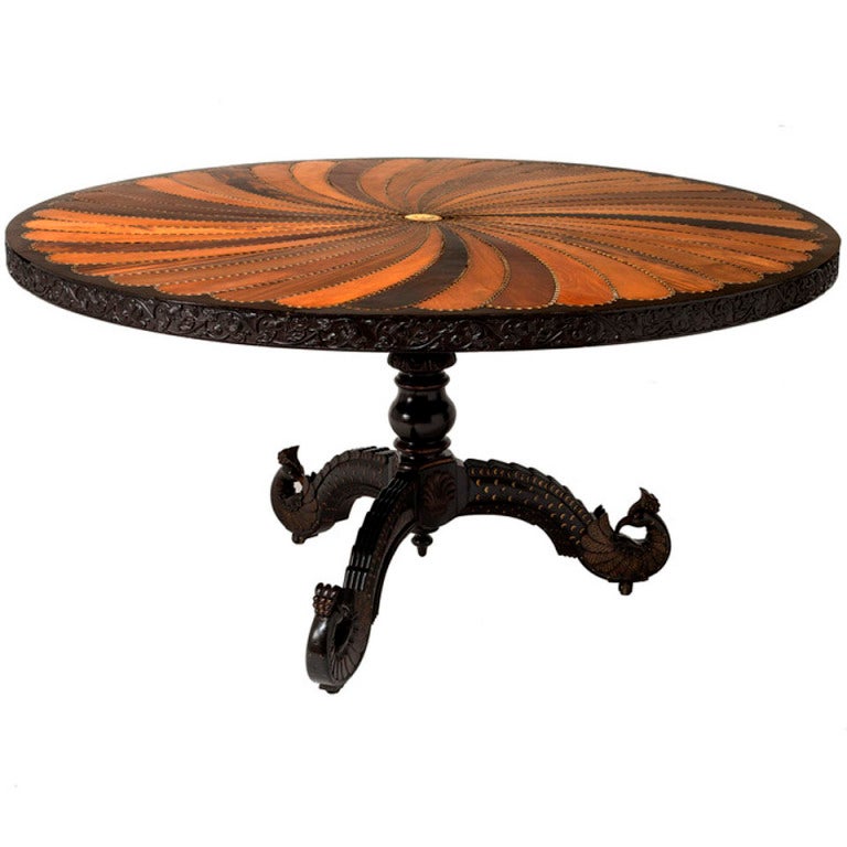 An Anglo-Indian carved and inlaid rosewood, ebony, hardwood, mahogany, bone and ivory circular center table.  The top formed of spiraling petal form inlays of exotic woods with a foliate carved frieze and distinctive peacock feet.  Provenance: A