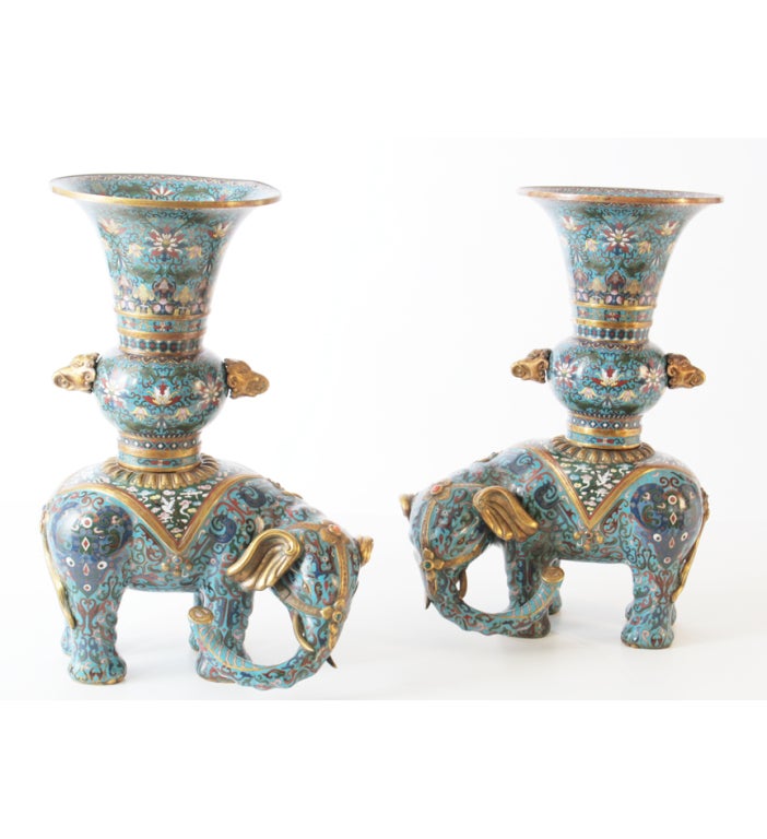 A pair of Chinese cloisonne enamel elephants, each standing four-square supporting a large vase, the elephants decorated with stylized archaistic animals and birds on a turquoise ground and wearing green saddlecloths patterned with cranes amongst