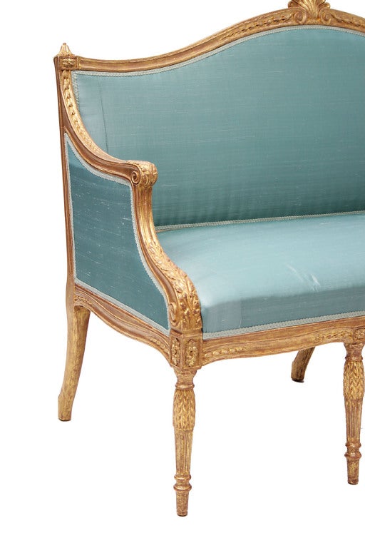 A George III giltwood settee with a shell-carved crest rail above a padded back and seat and with foliate carved arms, raised on tapering leaf carved legs; the seat inscribed '217 Hornby', possibly the name of the cabinet-maker.  A very similar pair