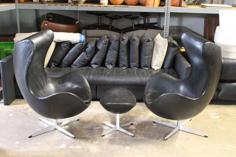 A pair of egg chairs and ottoman in original black leather. Designed by Arne Jacobsen for Fritz Hansen.