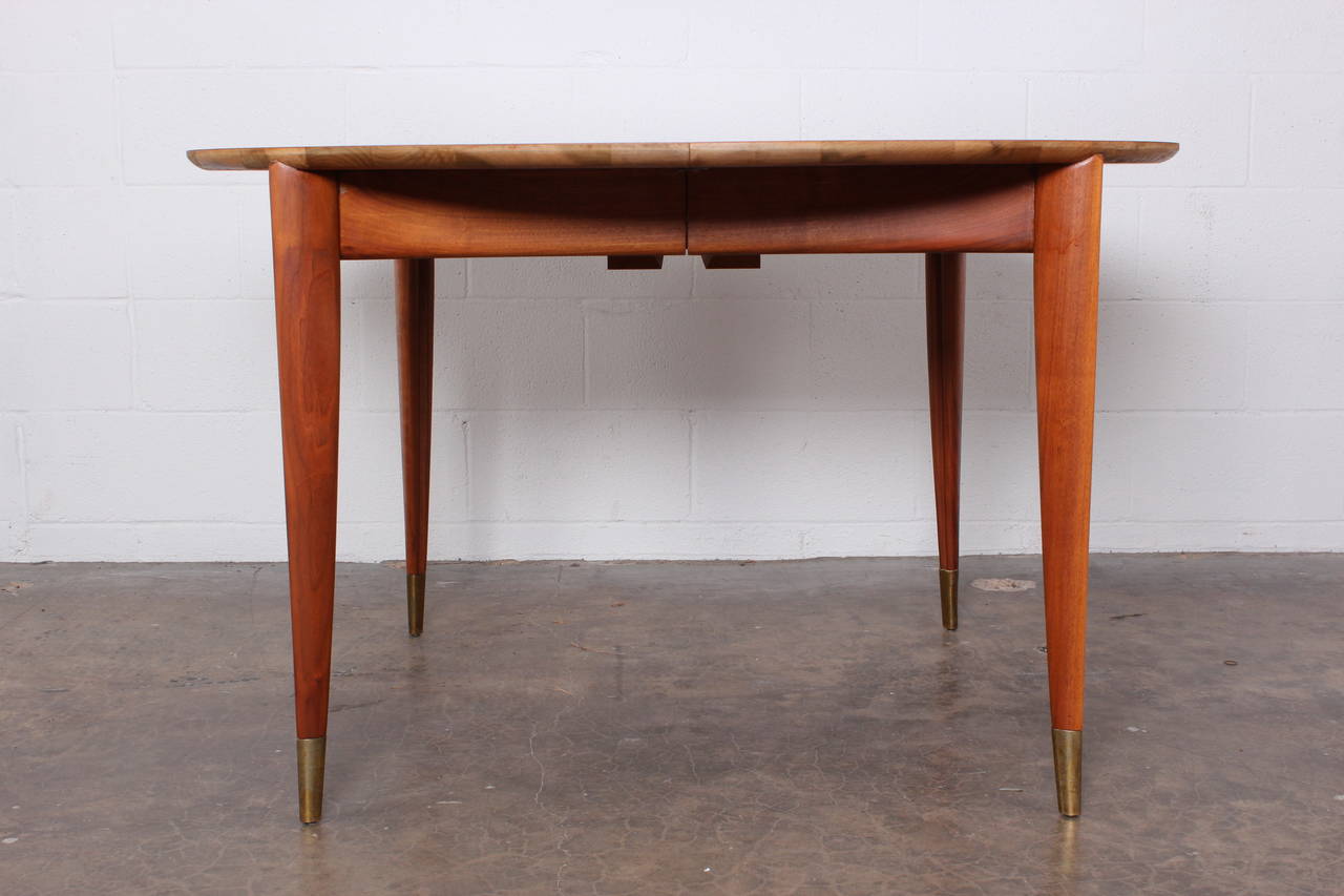 A large walnut dining table with brass sabots. Designed by Gio Ponti for Singer & Sons. Round table with four 14