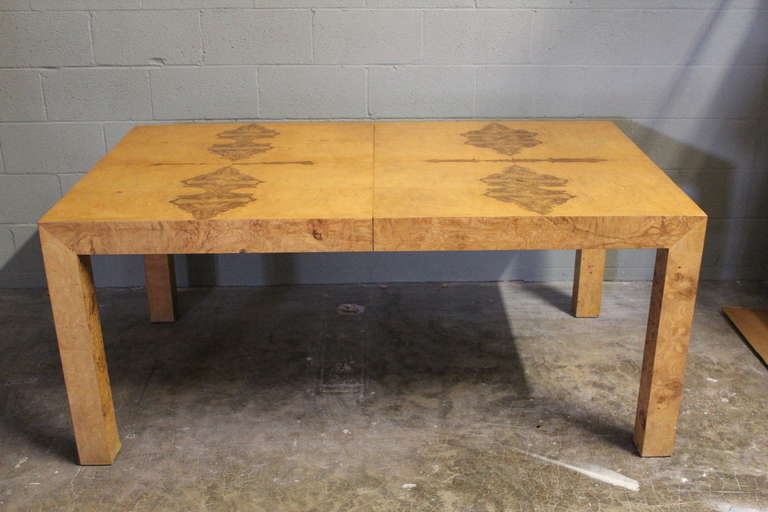 A large burl wood parsons dining table with two leaves. Designed by Milo Baughman for Thayer Coggin. The table measures 66 x 39 x 29(h) and has two 22