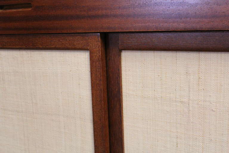 A mahogany credenza with sliding grasscloth covered doors. Designed by Edward Wormley for Dunbar.