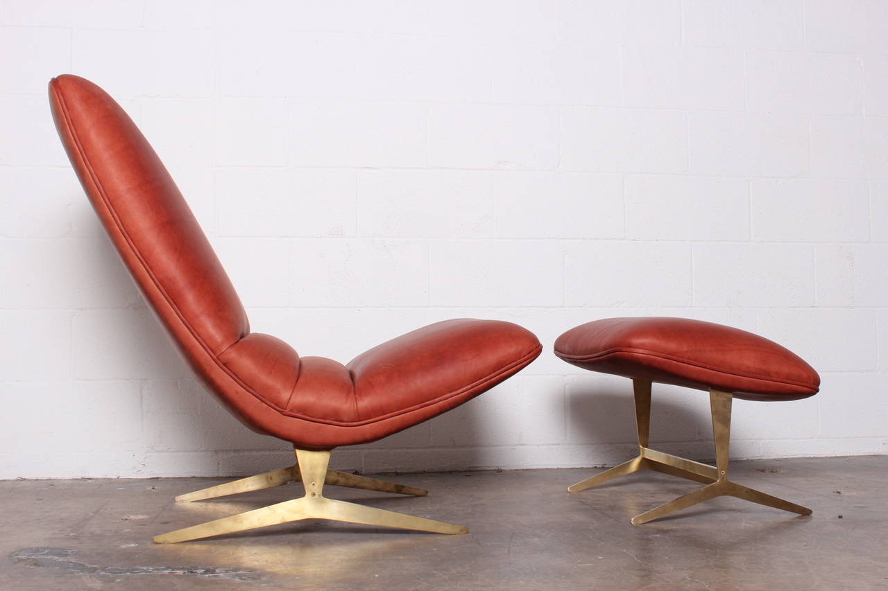 A leather lounge chair and ottoman on sculptural brass base.