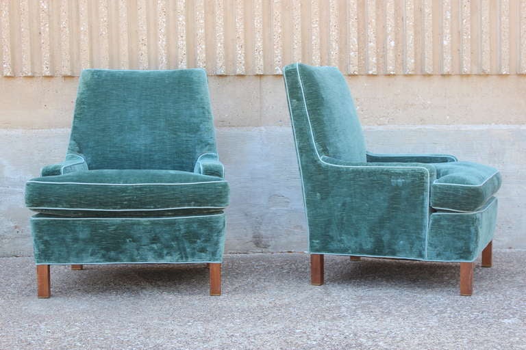 A pair of low arm lounge chairs with mahogany legs and brass feet. The chairs are wedge shaped with down cushions. Designed by Edward Wormley for Dunbar.