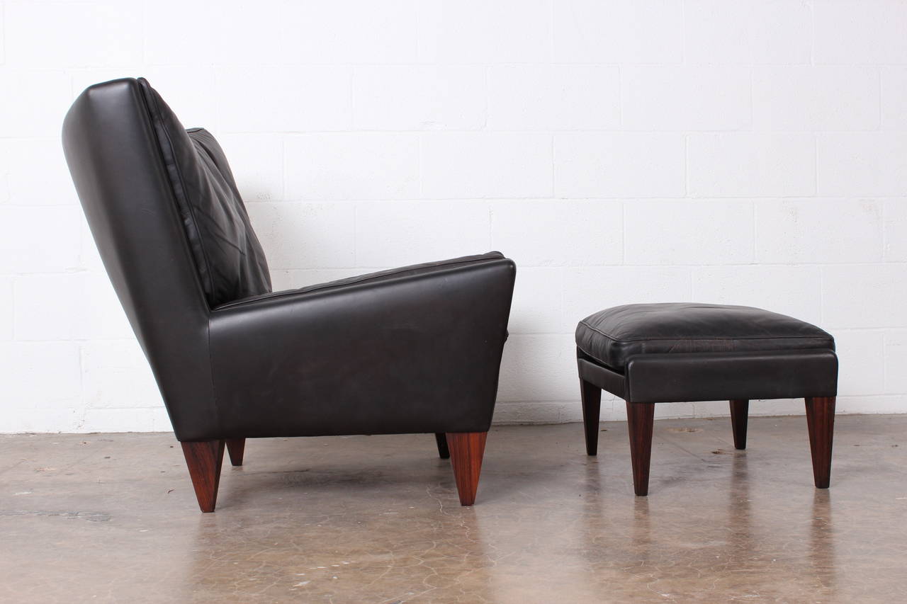 A pair of large-scale lounge chairs and ottomans in dark brown buffalo leather with down cushions and rosewood legs. Designed by Illum Wikkelsø. Sold individually. Matching sofa also available.