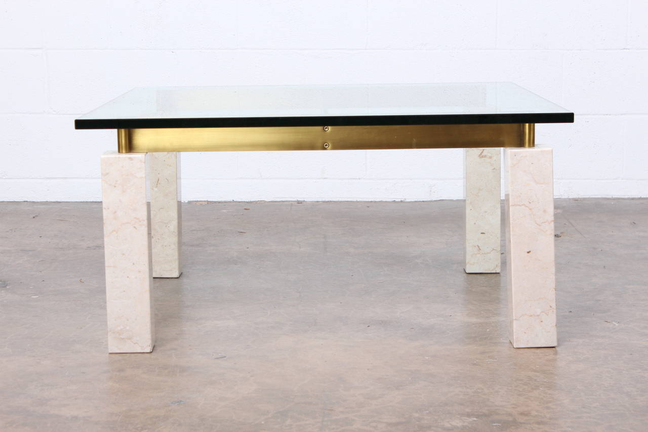 An architectural coffee table with solid travertine legs, solid brass stretchers and glass top.