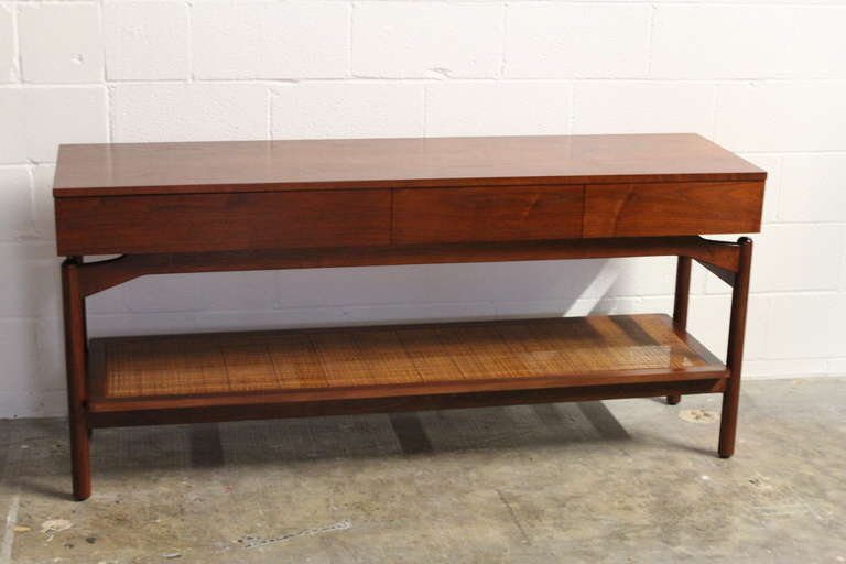 A walnut console table with three drawers and a cane shelf. Designed by Greta Grossman for Glenn of California.