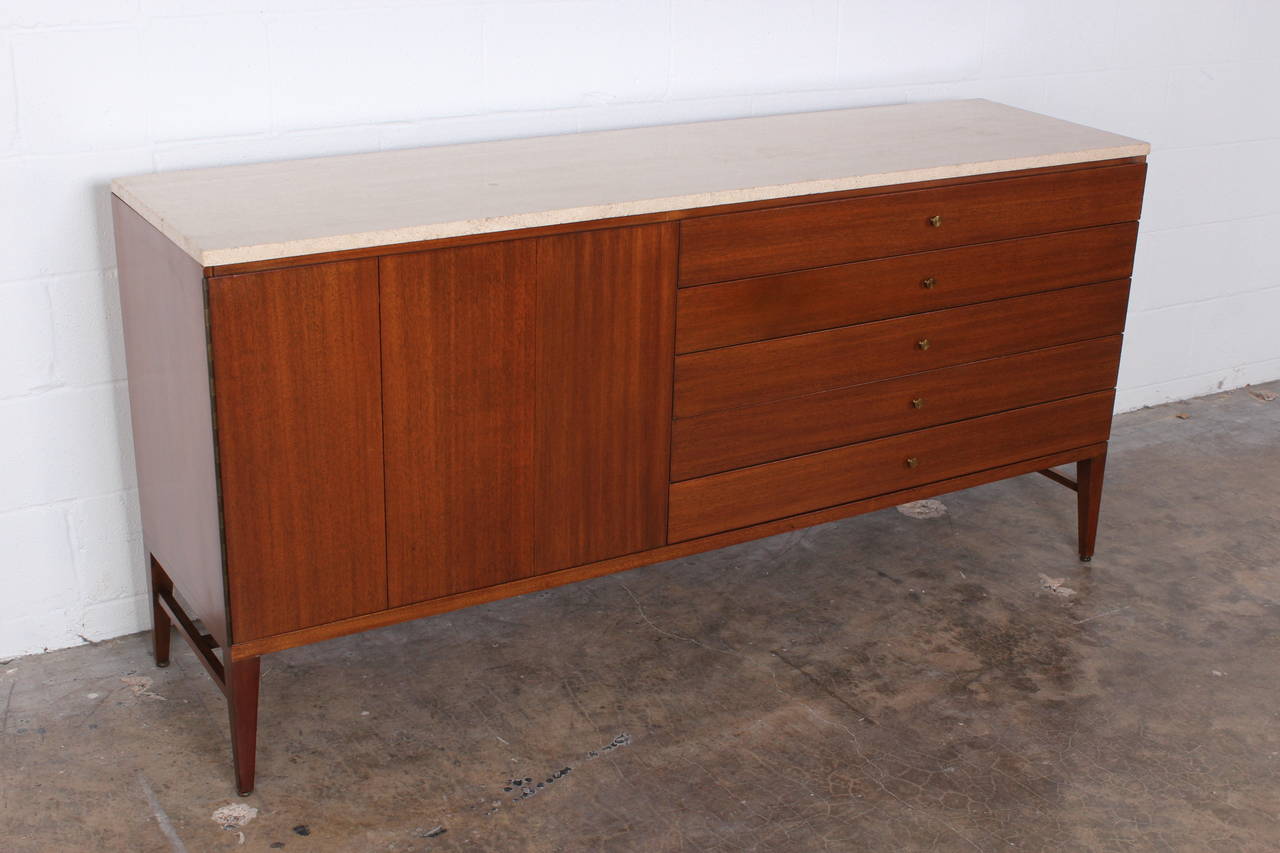 A mahogany cabinet with brass hardware and a travertine top. Designed by Paul McCobb for Calvin.