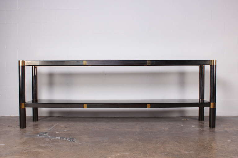 A large gunmetal and brass console table with smoked glass shelves. Designed by Karl Springer.