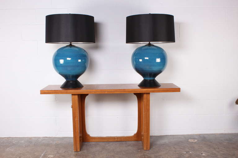 A large pair of beautifully glazed blue table lamps with black wooden bases and linen shades.