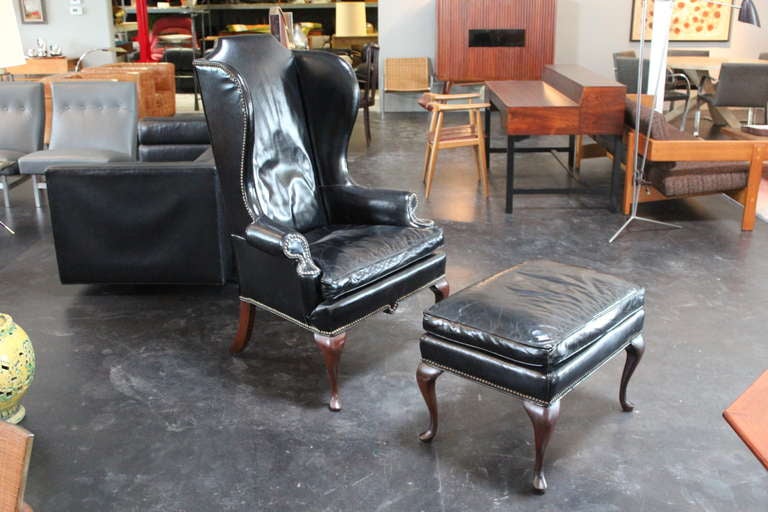 A generously scaled wingback chair and ottoman in original black leather with rich patina.