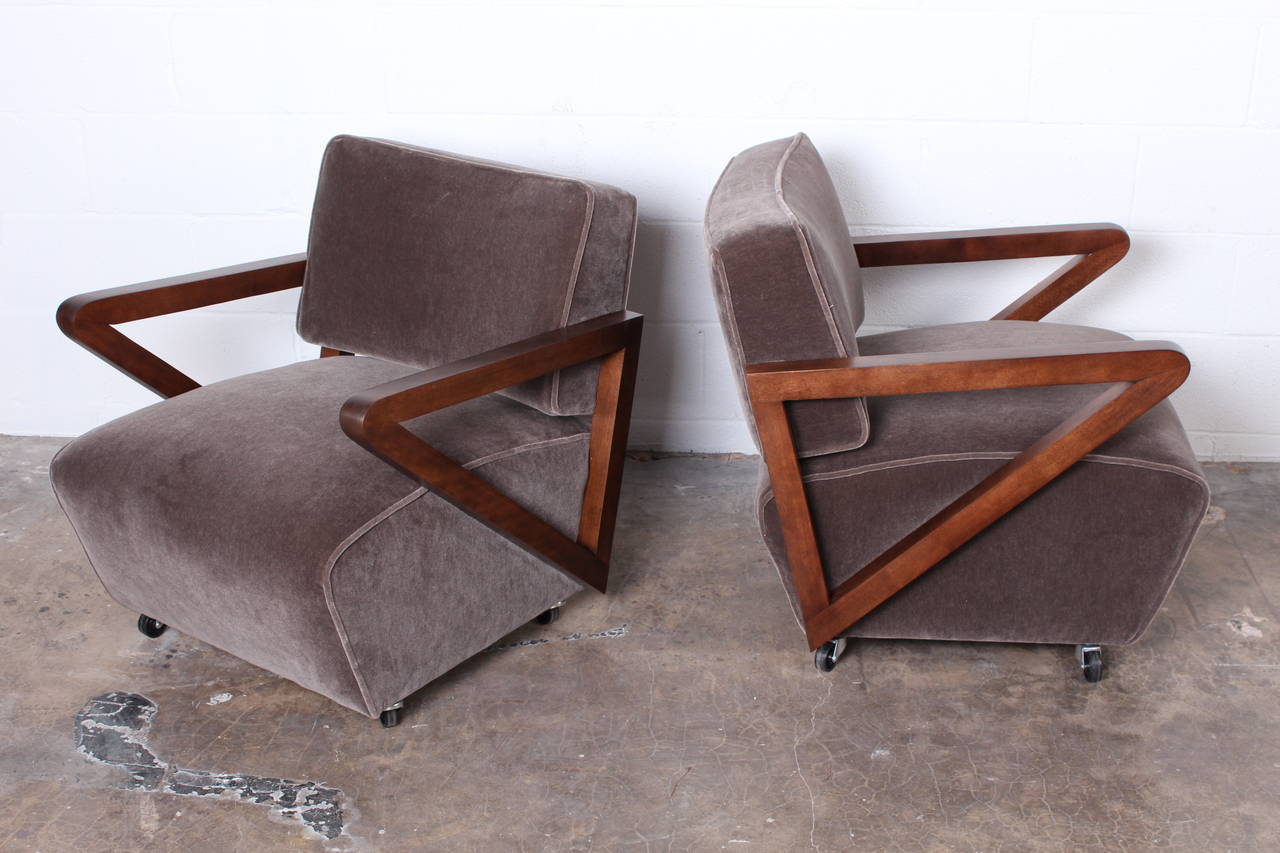 A pair of angular lounge chairs on casters with walnut arms and mohair upholstery.