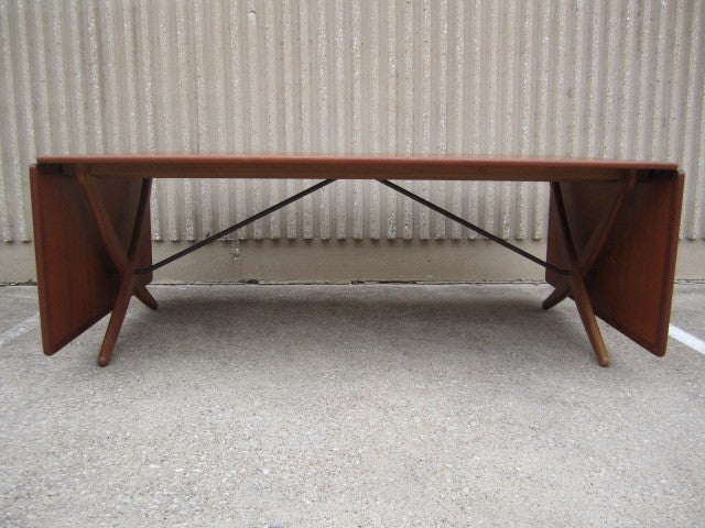 A rare find in this larger size. The Teak drop leaf table has a brass stretcher and oak supports that pull out to hold the leaves up. Table measures 76