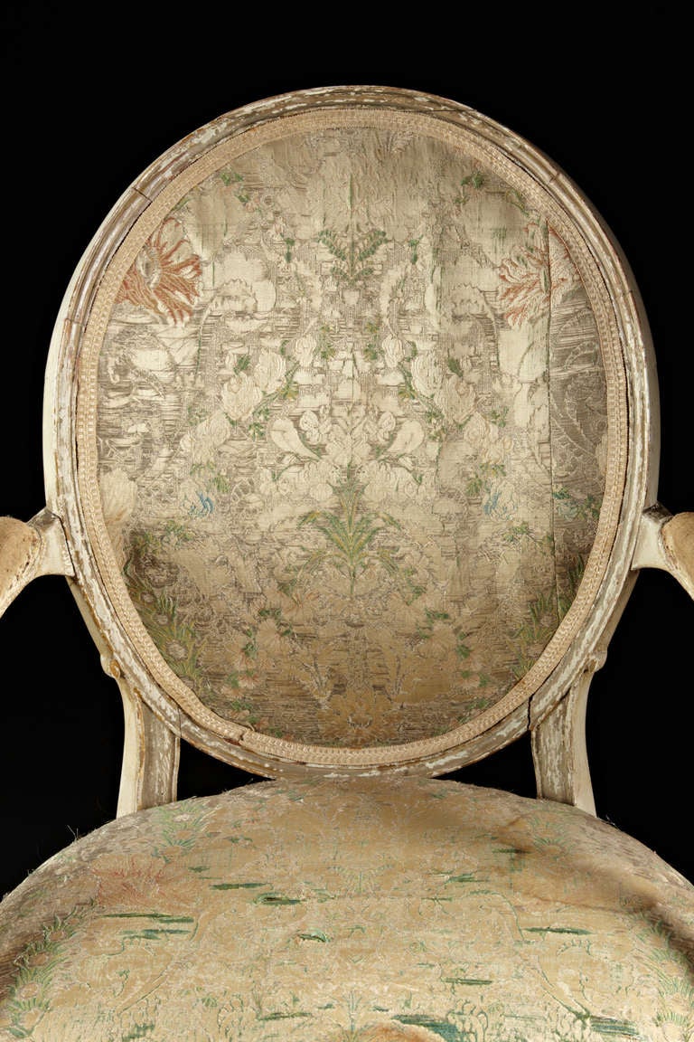 A pair of fine painted and gilt decorated Hepplewhite period armchairs with period silk lampas coverings. The oval backs are supported by curvilinear arms and molded seat frames on square tapered front legs and square raked rear legs. Original gilt