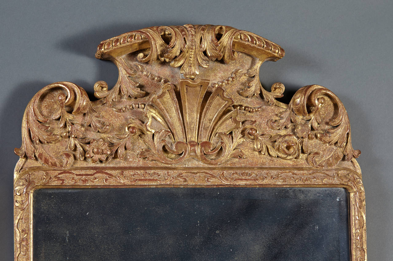 A fine and George II carved and gilt mirror with original bevelled plate and panelled back. The crest with carved central stylized plume is over a rectangular frame with strapwork and carved elements over a lower apron with applied rosettes and