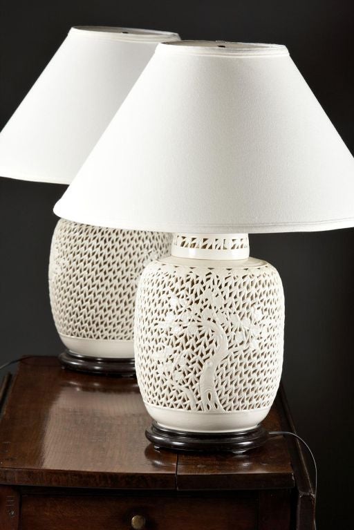 A pair of large reticulated white blanc de chine lamps, 20th century (Mid) with internal light and top lit with shade. The vine and floral pattern on a bulbous ginger jar shaped body raised on a conforming wooden base.