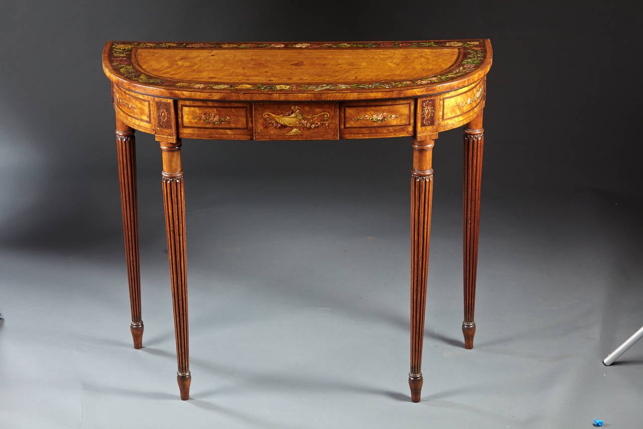 A very high quality English satinwood console or pier table having reeded turned legs supporting a “D” shaped top with painted and inlaid decoration. The frieze with aternating painted urn and rose panels. The crossbanded top is painted with rose