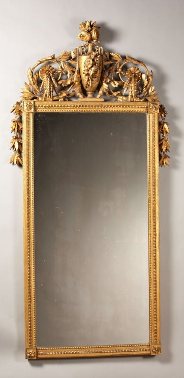 A finely carved giltwood pier mirror with urn top finial flanked by floral elements and leaf carved valences. The frame with rosette corners and beaded molding surrounds a rectangular plate. retains a very old, if not original, gilt surface.