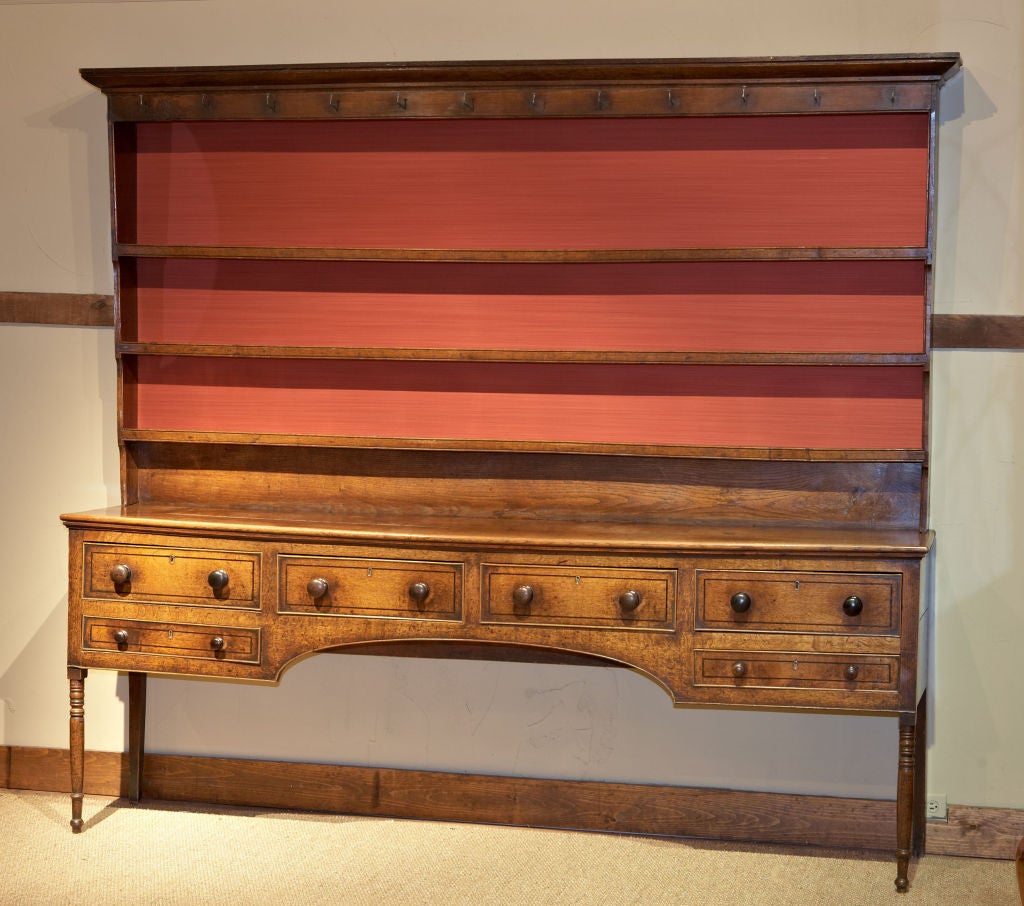 An impressive large scaled oak dresser of English origin, circa 1800-20. The upper plate rack with forged iron hooks rests on a base with two central inlaid drawers flanked by two end banks of double drawers supported by turned front legs. The