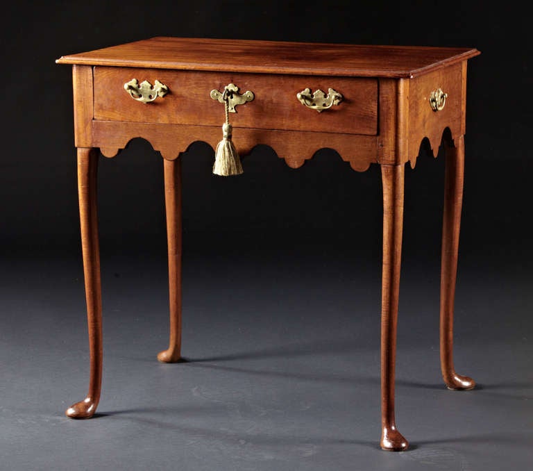A diminutive Queen Anne walnut or mahogany tea table with scalloped apron on all four sides and a single drawer on sculpted carved semi cabriole legs ending in slipper feet. Probably English, circa 1750.