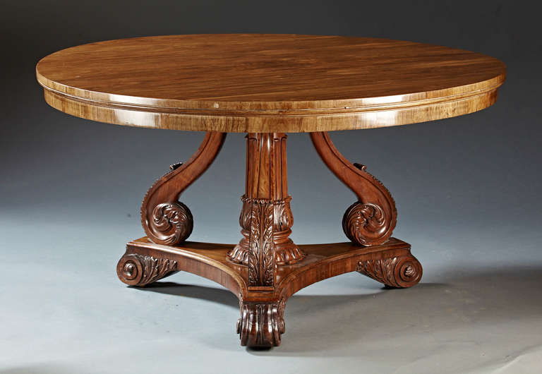 A large and finely figured and carved rosewood tilt top center table. The figural round top raised on a carved central column pedestal shaft resting on a trifoil base ending in carved scrolled feet with sunken casters. The select figural wood on the