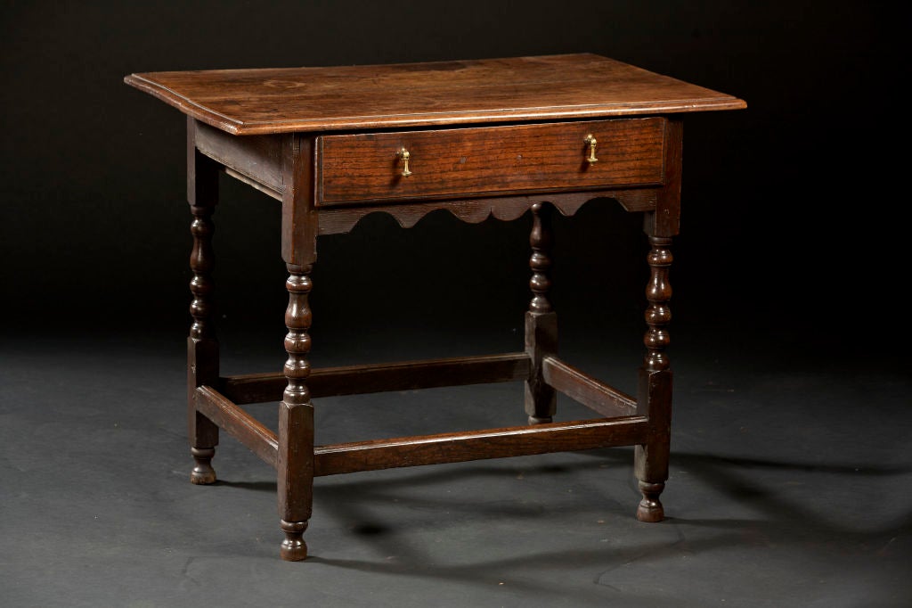 An elmwood tavern table with molded edge, rectangular top over a conforming case with single drawer supported by four turned block and vase shaped legs joined by a box stretcher. English, circa 1760.