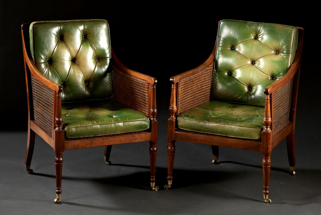 A pair of George III mahogany caned library bergeres. The rectangular curved backs and straight sides are caned with turned front posts and are supported by turned legs and raked square rear legs on casters. English, circa 1790-1810.