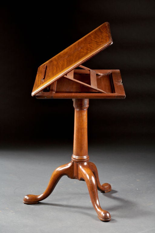 A George II mahogany reading stand or drafting table having a rectangular adjustable height top with ratchet mechanism and spring loaded book rest above a turned shaft on tripod base with cabriole legs and padded feet. English, circa 1750.