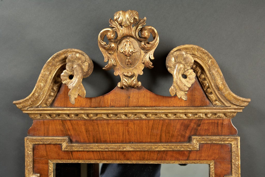 A George II walnut and parcel gilt carved mirror with shaped frame. The foliate carved swan's neck pediment with giltwood cartouche is over a walnut veneered framework having imbricated and egg and dart molded edging and with foliate carved giltwood