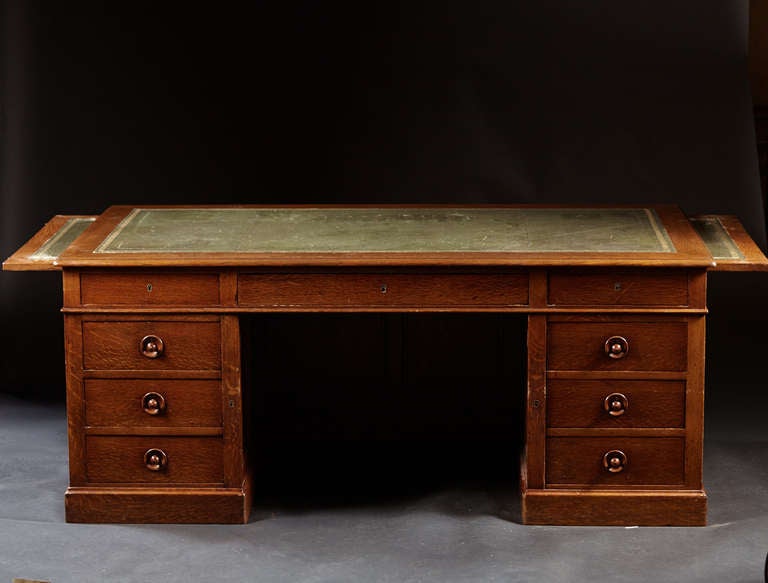 A large scaled oak pedestal desk with graduated locking drawers and leather top. The size of the work space is further enhanced by side slides also with leather surfaces for office use. This generously proportioned desk was made in the latter part