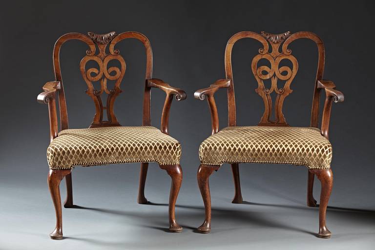 A wonderful pair of walnut George II period armchairs with interlaced carved and incised back splats within incurved stiles supported by scrolled arms over broad upholstered seats raised on cabriole legs in front and raked rear legs. The openwork