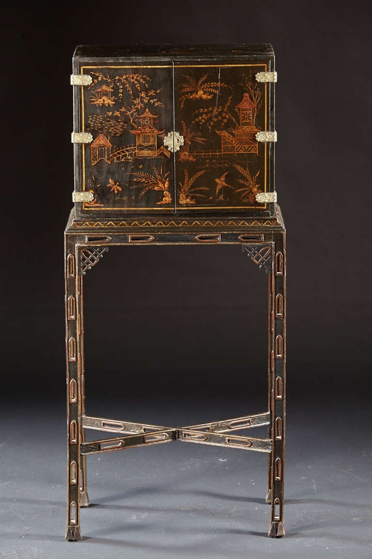 A diminutive lacquered cabinet on stand having raised gilt  and line decoration on sides and double doors opening to a similarly decorated interior with multiple drawers. The cabinet raised on a later pierced base with cross stretcher and paint