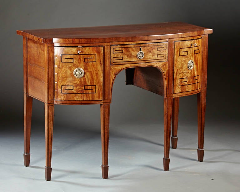 A fine English mahogany sideboard from the Regency period. The projected bowfront above a central inlaid drawer flanked by unusual large swivel cabinets inlaid on front and back surfaces and the whole raised on square tapered and line inlaid legs