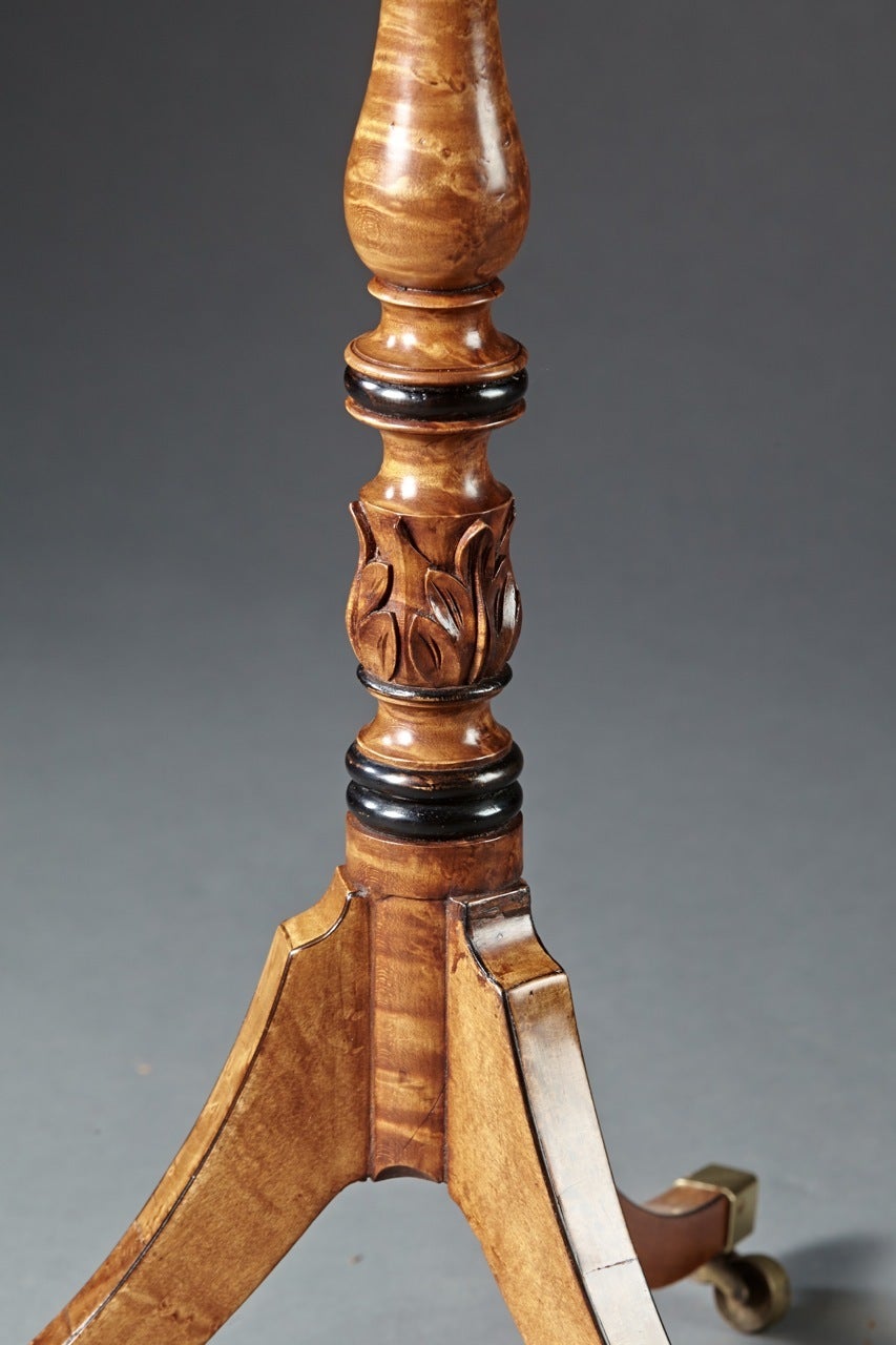 A finely carved and finished English bird's-eye maple stand. Of very high quality, the inlaid and chamfered corner top above a turned and carved shaft with a tripod base ending in brass casters. The top retaining its wood screw for detachment.