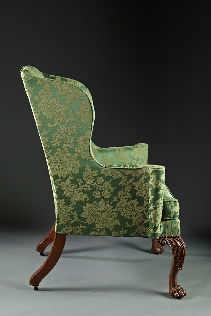 A walnut George II wing chair with deeply carved cabriole front legs ending in lion paw feet and having great proportion and accentuated acanthus carved knees. The rear legs are square and out swept. Overall with great poise and presence, this chair