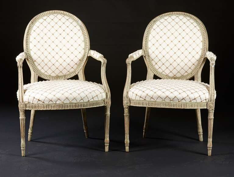 A pair of white painted, oval back fauteuils with fluted frames on over-upholstered seats with turned and carved legs from the Hepplewhite period. The surface has been cleaned to the original painted surface and now has the pleasing continuity of a