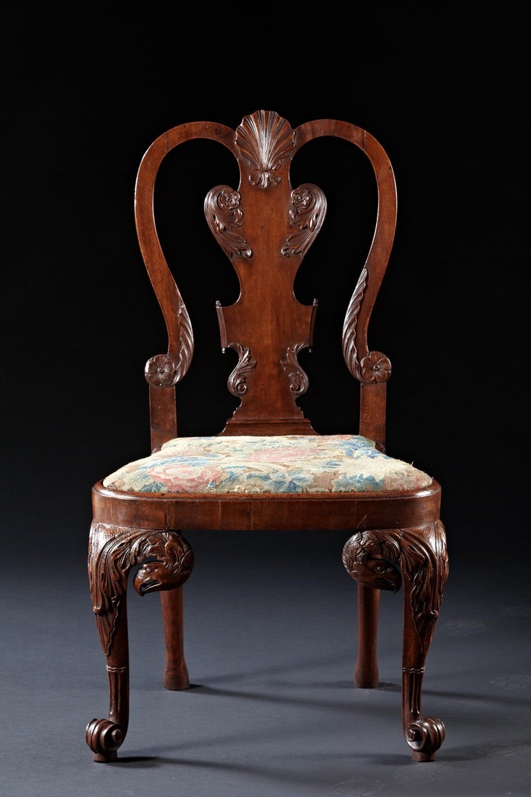 A rare pair of walnut shell and eagle carved side chairs with petit pointe needlepoint seat covers. The conchoidal emblem of St. James on in-curved backs with delicately carved appliques of rosettes and acanthus leaves flank solid splats over bell