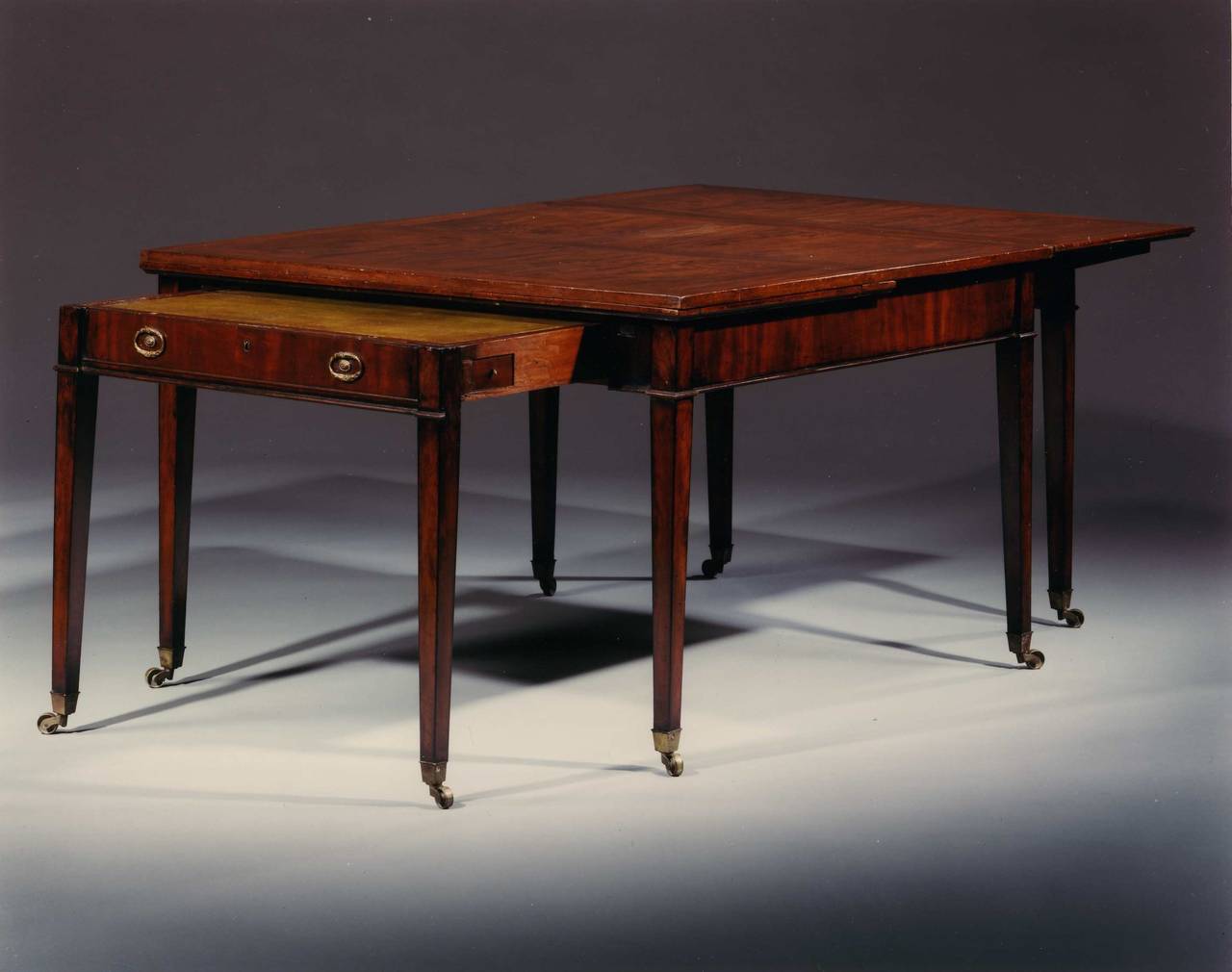 English mahogany neoclassic Sheraton design period table with pull-out leaves and leather top writing surfaces below the leaves to either side. When closed may be used as an extending dining table. The desk compartments are pulled out separately