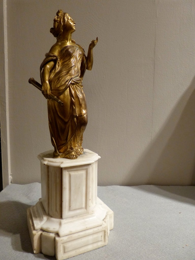 A fine quality French neoclassic allegoric female figure in gilt bronze, holding a telescope and looking up to the skies, alluding to the sciences, on  a stepped Carrara marble base. Early 19th century. Circa 1820.