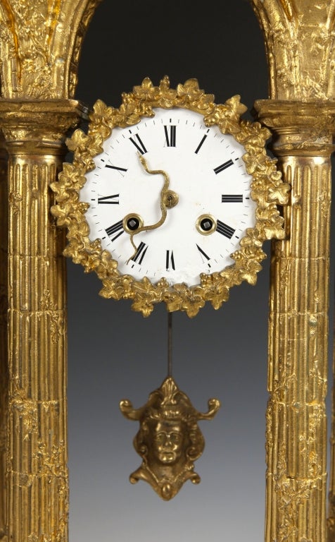 A fine and unusual French early 19th century ormulu neoclassical clock in the form of a Roman ruin, the face with serpent shaped hands, Egyptian motif pendulum and floral wreaths around the face.