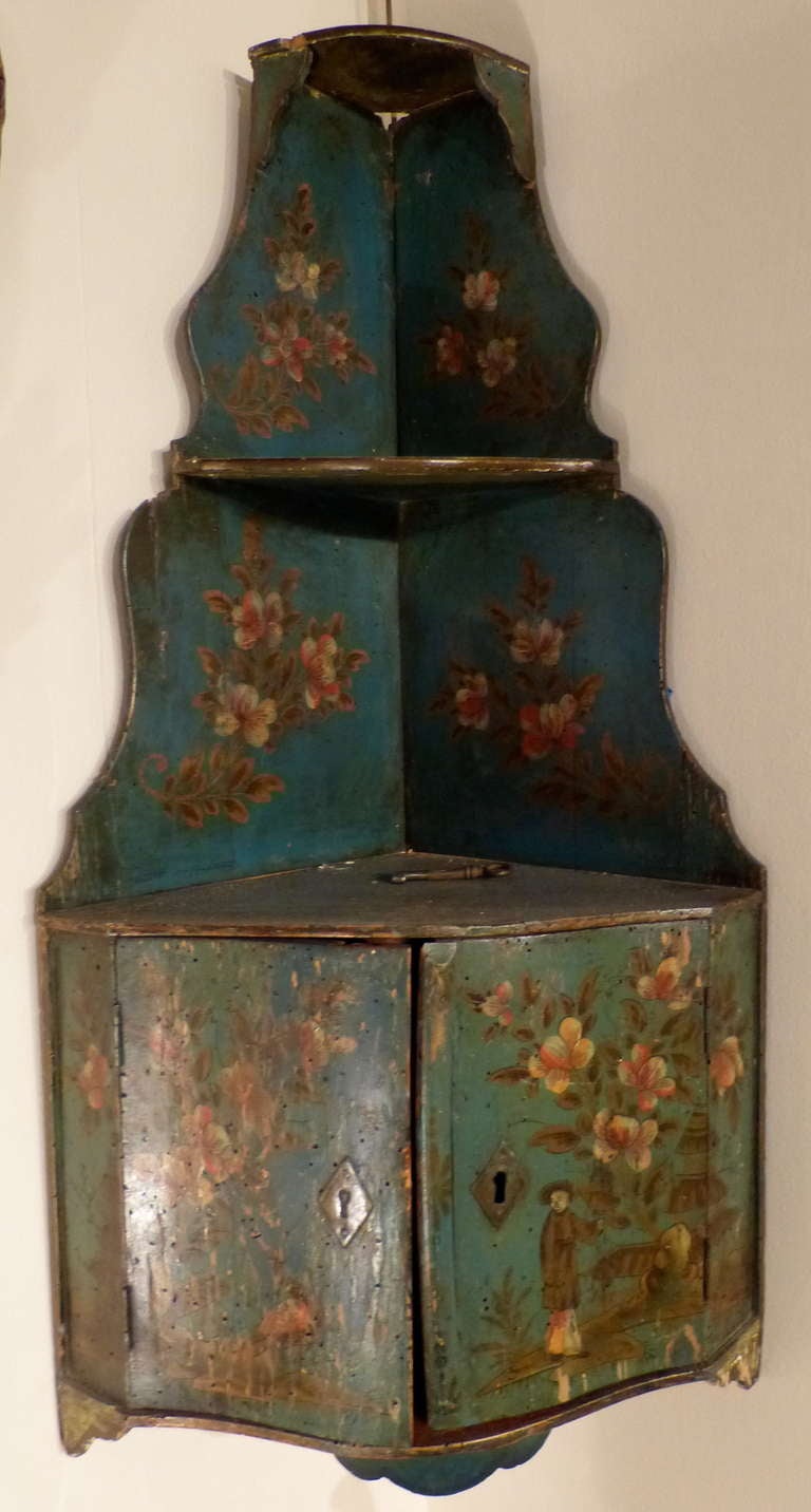 A good Italian chinoiserie painted hanging corner cupboard with serpentine front doors below shaped two-tier shelves with floral painting. The paint is original 18th century.