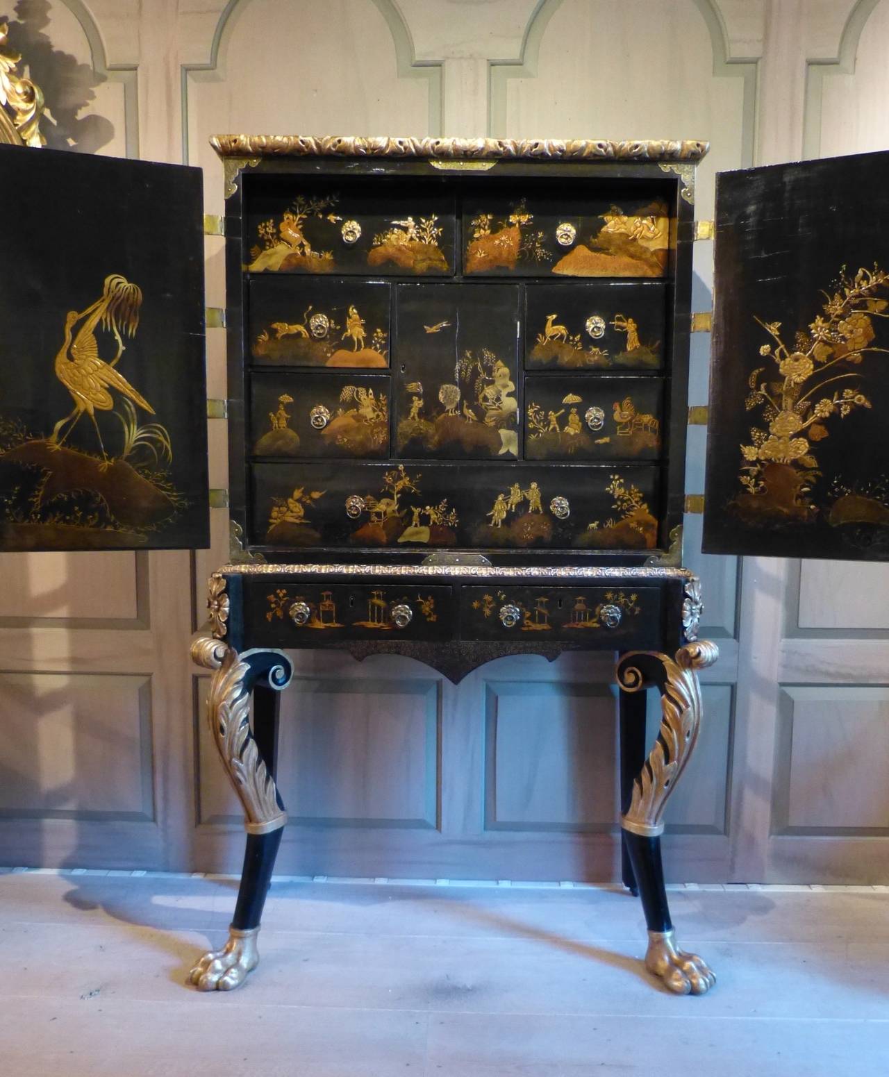 A fine Chinese export lacquer cabinet on Regency period carved ebonized and giltwood stand ending in lion's paw feet. The interior fully fitted with a bank of drawers displaying various scenes. The inside of the doors with a Fine depiction of a