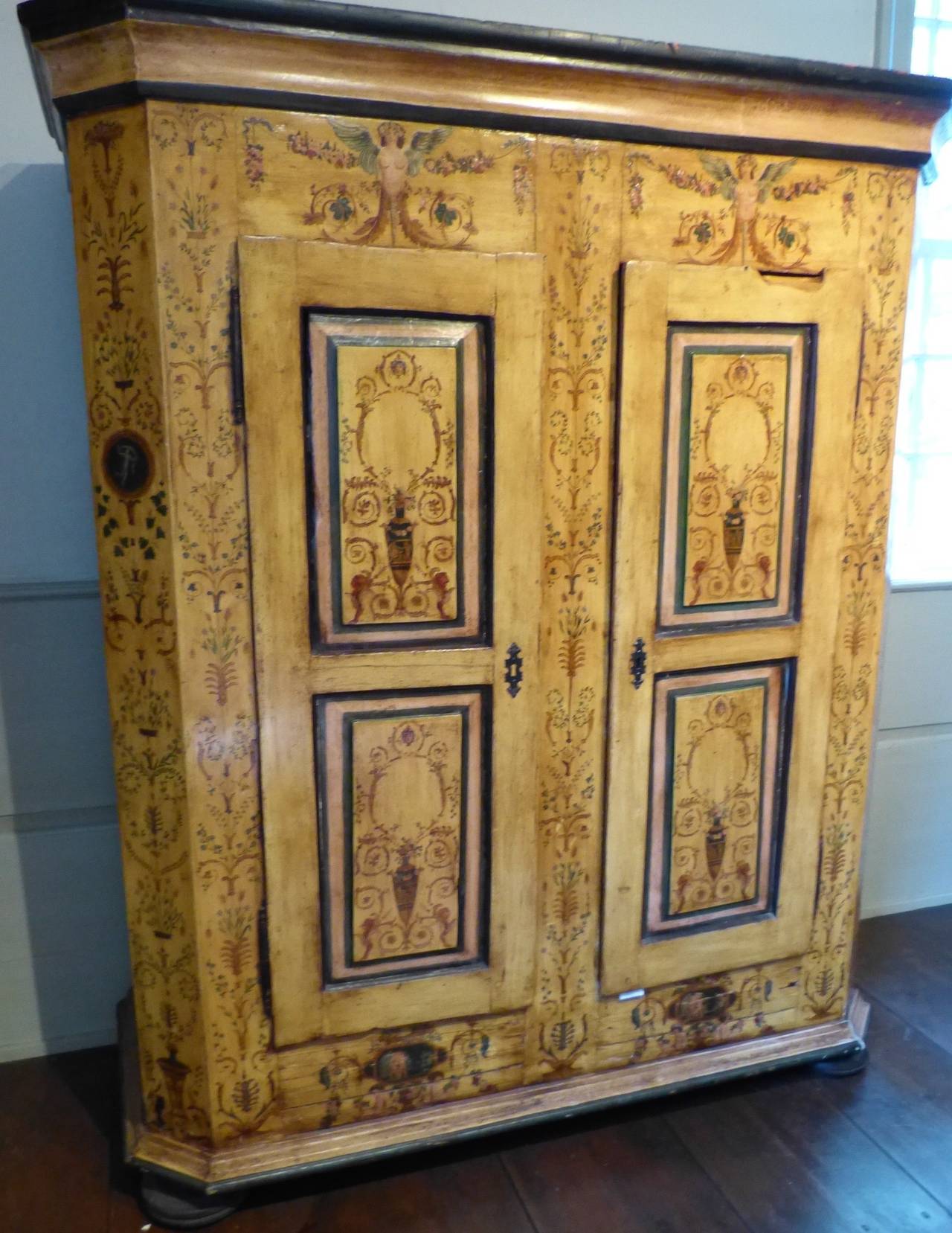 The molded cornice over two paneled doors flanked by canted angles, raised on bun feet, the whole well painted all-over to show flowers, classical vases, sphinxes and laurel sprays, 18th century, circa 1770.