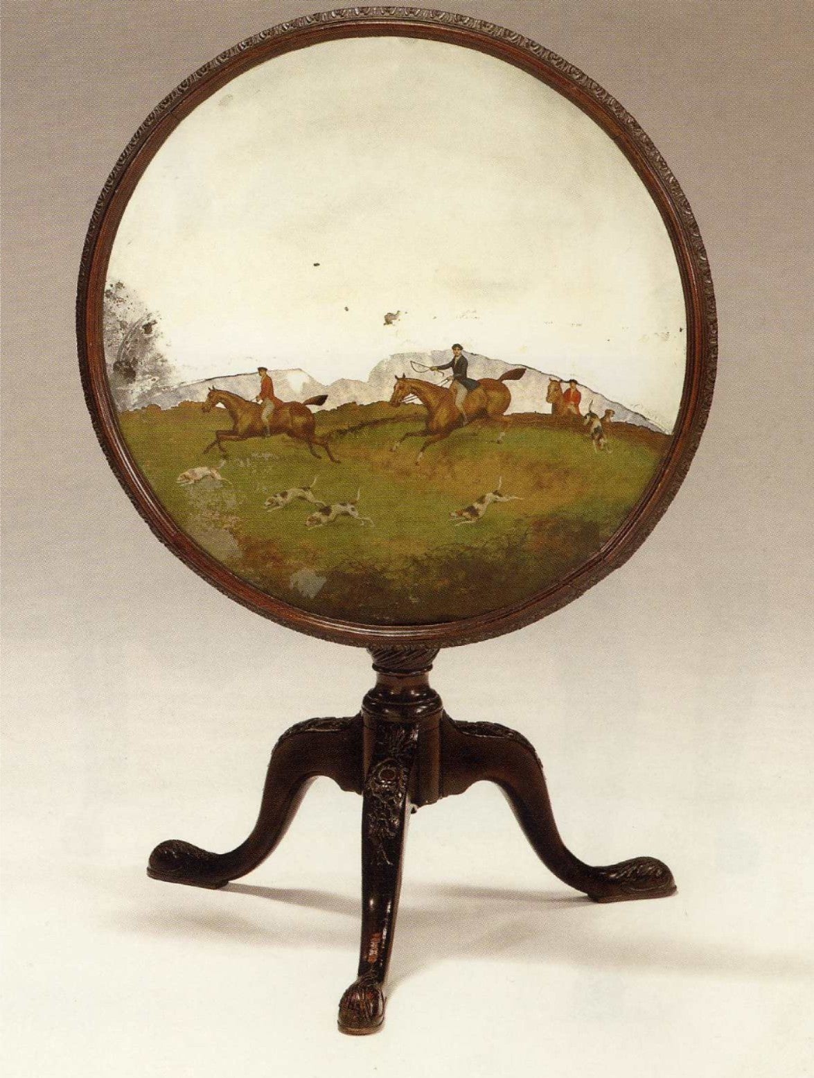 Rare mahogany 19th century tripod table with reverse painted glass top. The circular top with foliated carved edge centered by a panel of reverse painted mirror glass depicting a scene from a fox hunt. The carved tripod base with vase shaped stem