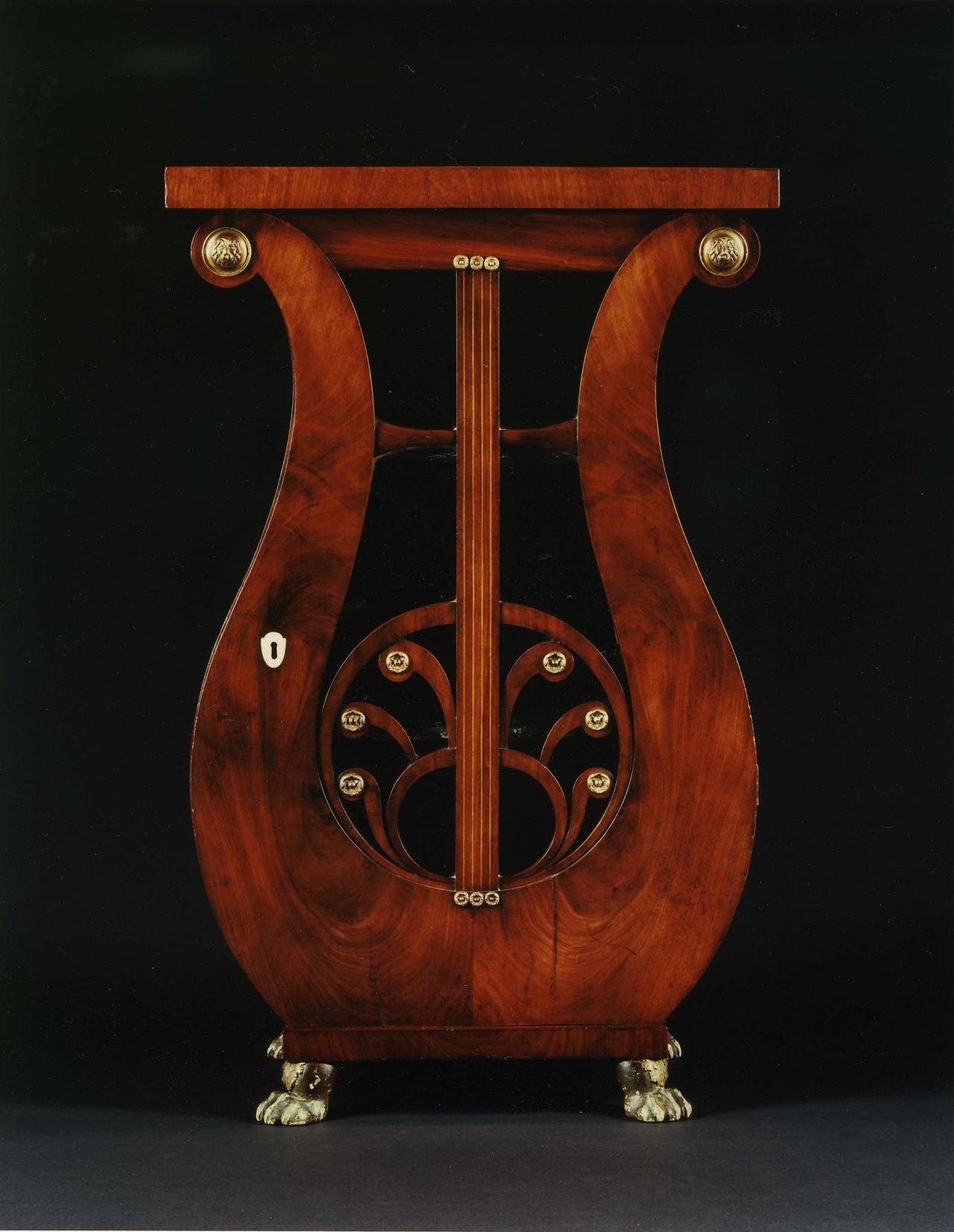 A highly unusual pair of mahogany lyre shaped pedestals mounted with lacquered brass. Each with rectangular top resting on a lyre-shaped body with glazed door with inlaid strings and paterae. Enclosing shelves, on bronzed paw feet, German, circa