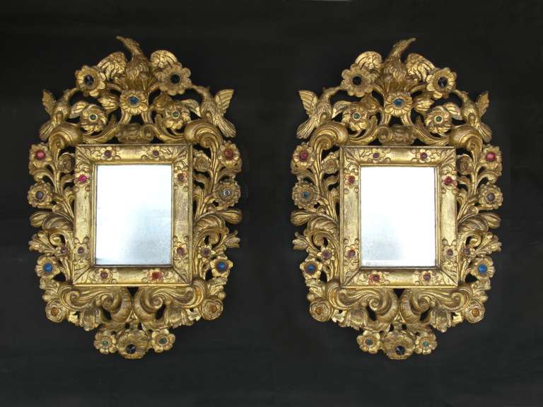 Rare and unusual pair of small, vividly carved gilt frames featuring flowers adorned with colored glass jewels and three birds forming the crests. Old and slightly distressed mirror plates.
